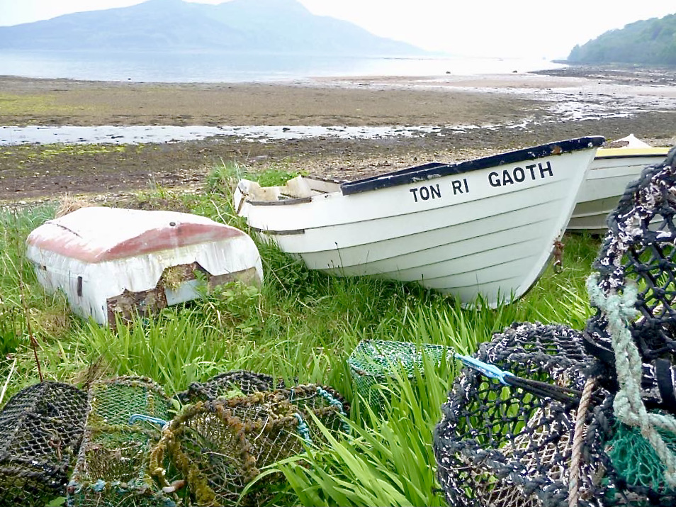 A photo of boats pulled up on the Shore at Lamlash. Holy Isle can be seen in the background.