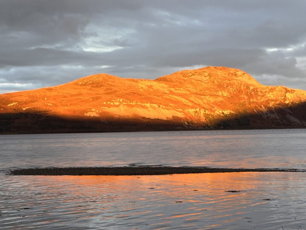 A photo with bright sun shining on Holy isle, with dark clouds in the background, creating strong contrast and shadow.