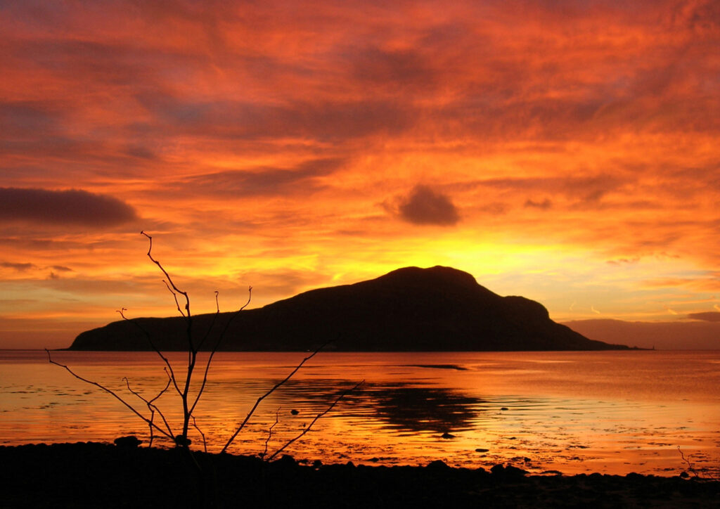 A vivid photo, with orange coloured clouds, of sunrise over Holy Isle