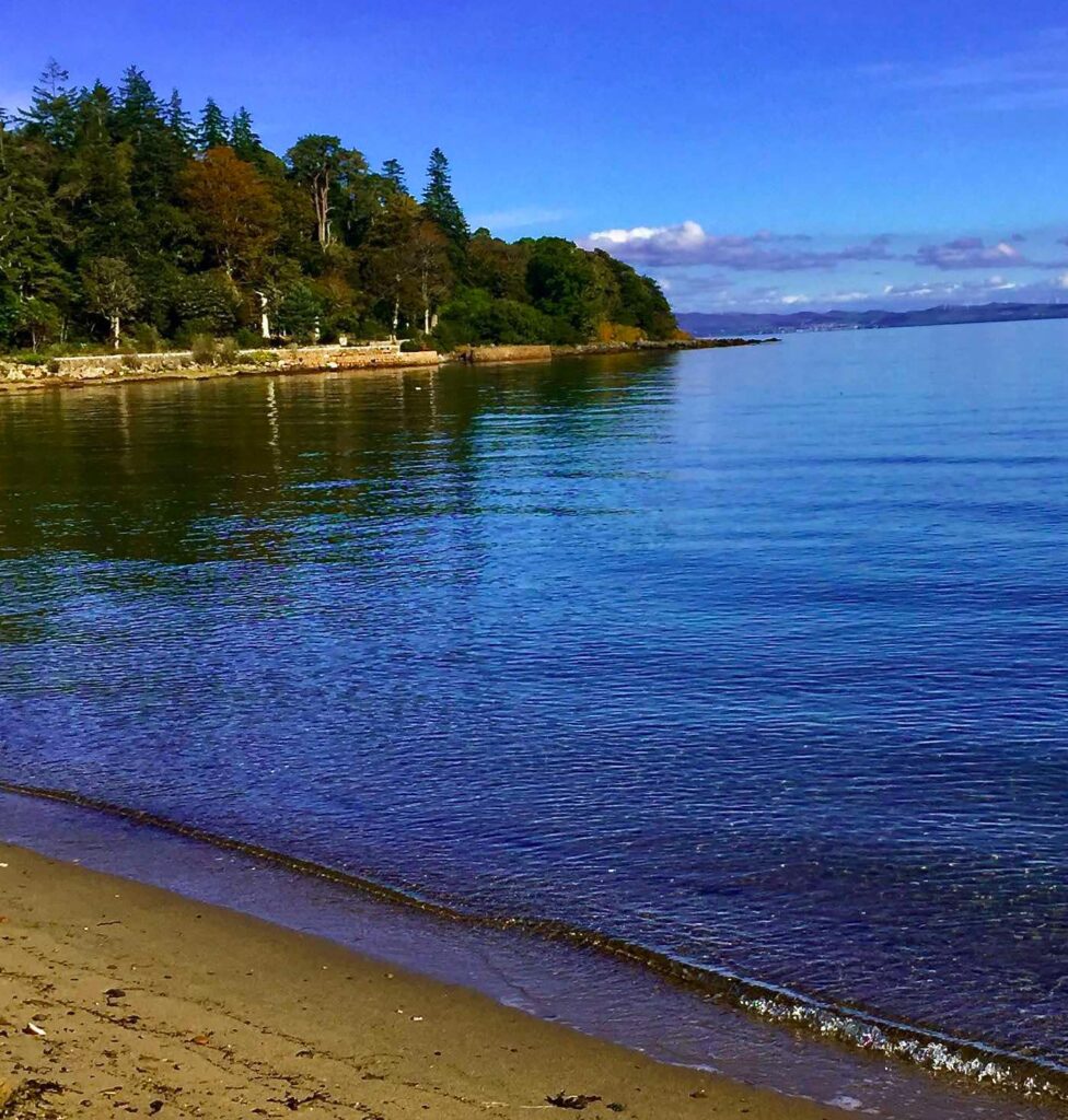 A photo from Brodick bay beach, with the trees below the castle in the background